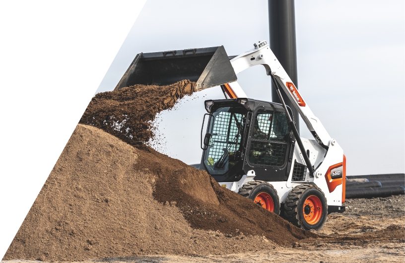 Compact skid steer dumping dirt onto a dirt pile.